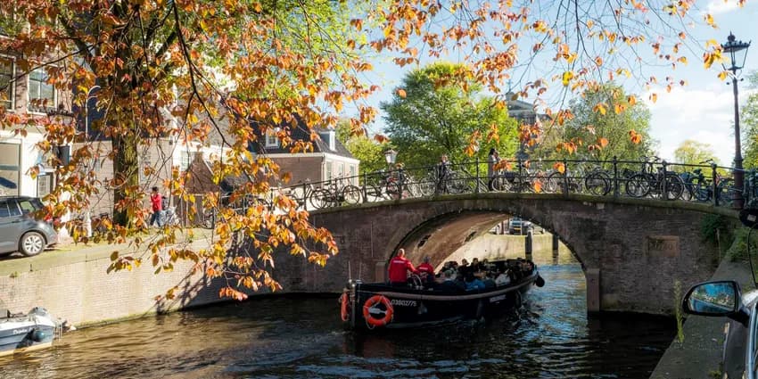 A tour boat passing by under the bridge on a sunny autumn day on Reguliersgracht.