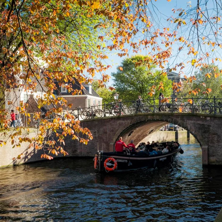 A tour boat passing by under the bridge on a sunny autumn day on Reguliersgracht.