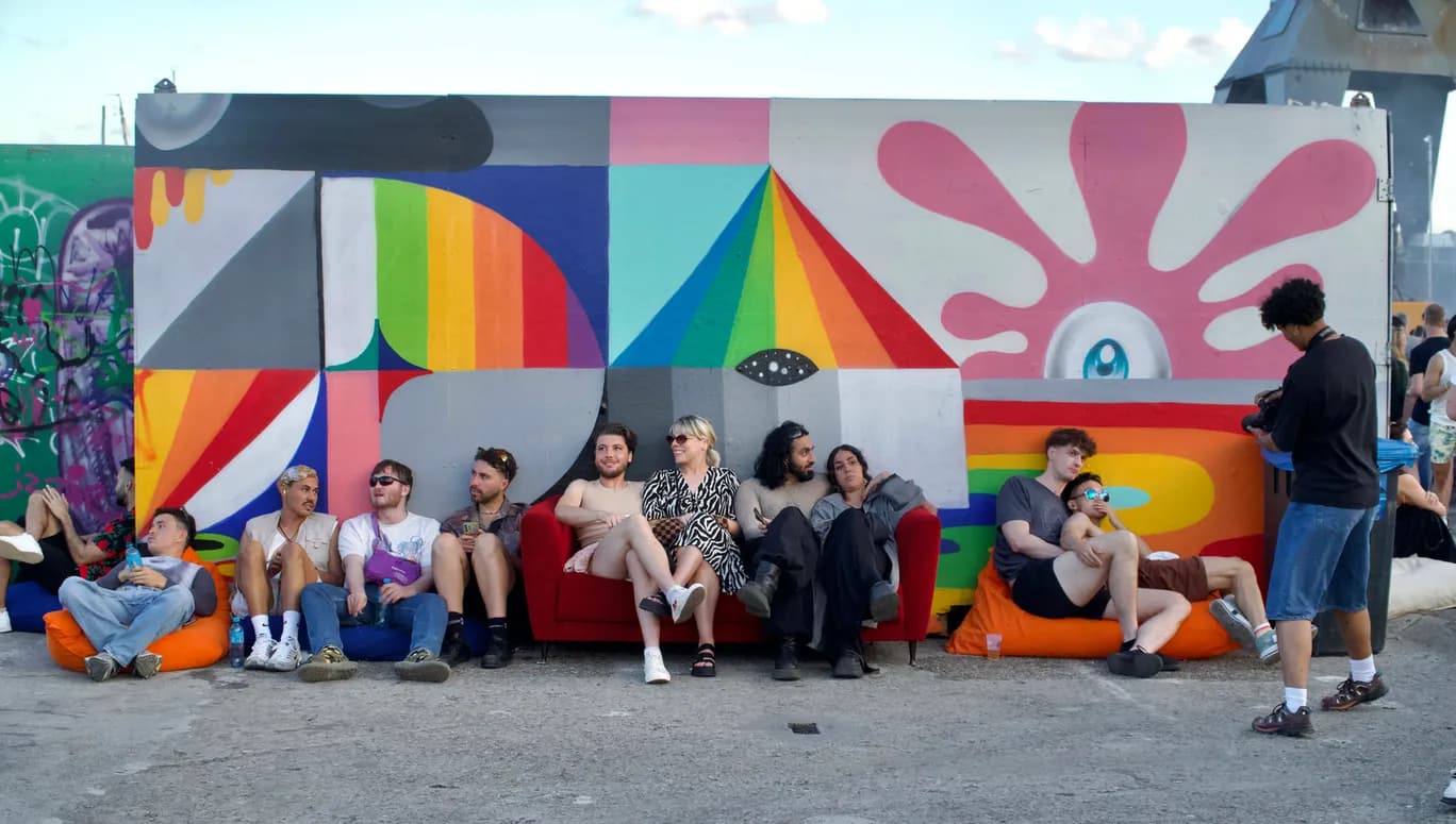 People lounging next a colourful wall at Tropikali Festival 2024.