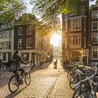 Amsterdam, Netherlands - September 22, 2021: Early morning in Amsterdam. Artistic image. People ride bicycles, the ancient European city of Amsterdam. Sunlight and silhouettes, beautiful downtown houses. Amsterdam, Holland, Netherlands, Europe