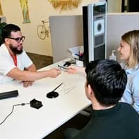 Man and woman sitting at a desk in the INAmsterdam offices, employee handing over an id card