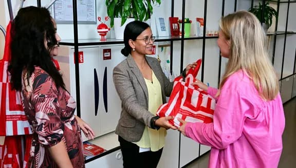 Two women in the INAmsterdam offices, receiving an INAmsterdam tote bag