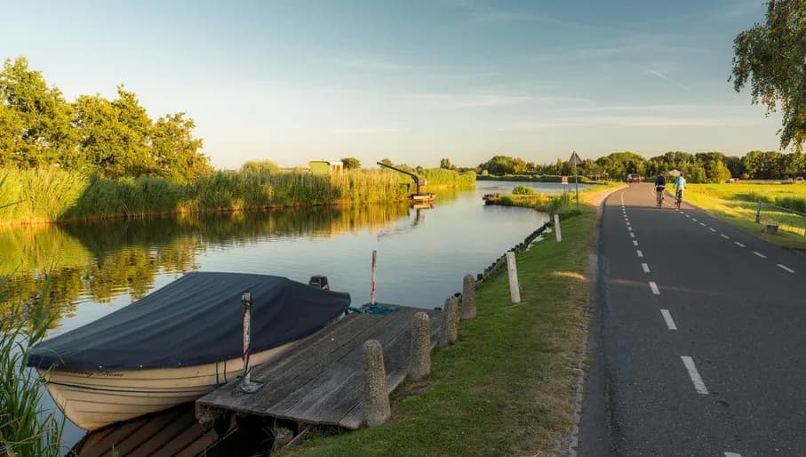 A boat in the water and two cyclist passing through the Goois Nature reserve.